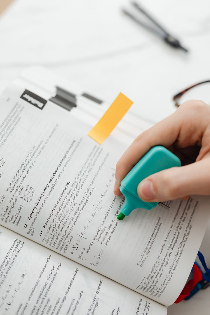 Services Hand using a green highlighter to mark text in a textbook with page markers.